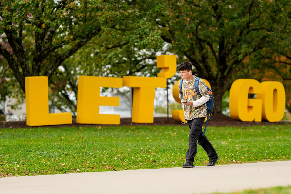 A student walks past giant gold letters that spell "Let's Go"