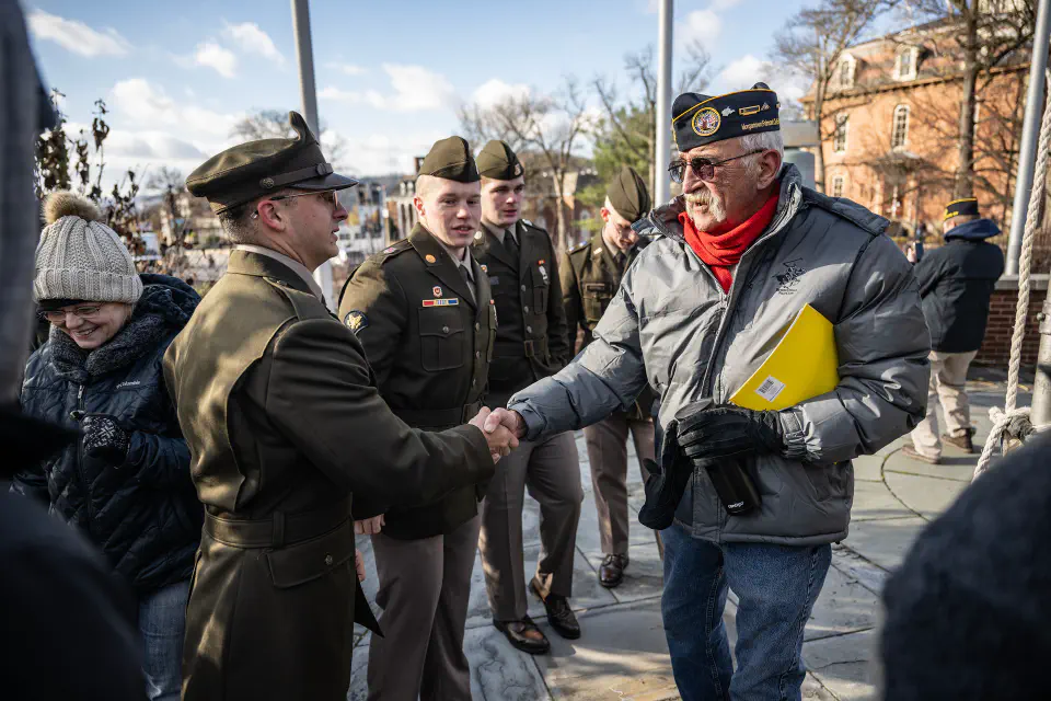 A military veteran shakes the hand of a younger man in a military uniform outside of Oglebay Hall on the Downtown campus.