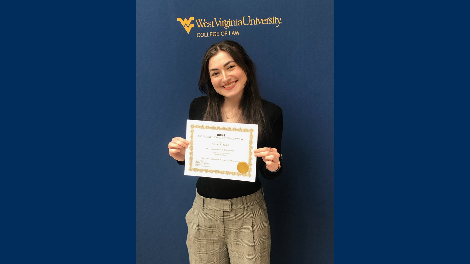 Photo of Abigail Paugh holding a certificate in front of a WVU backdrop.