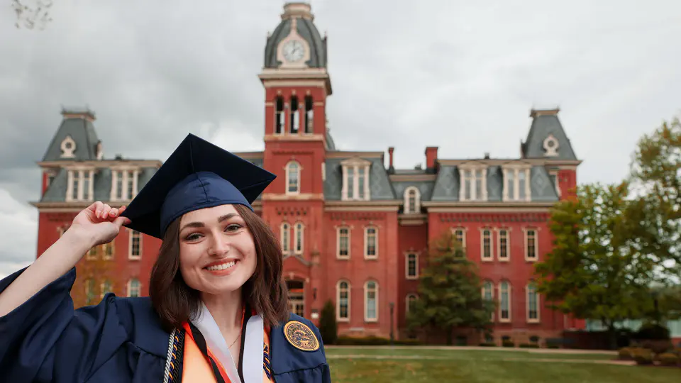 Abbigail stands in front of Woodburn hall in her blue graduation cap and gown.