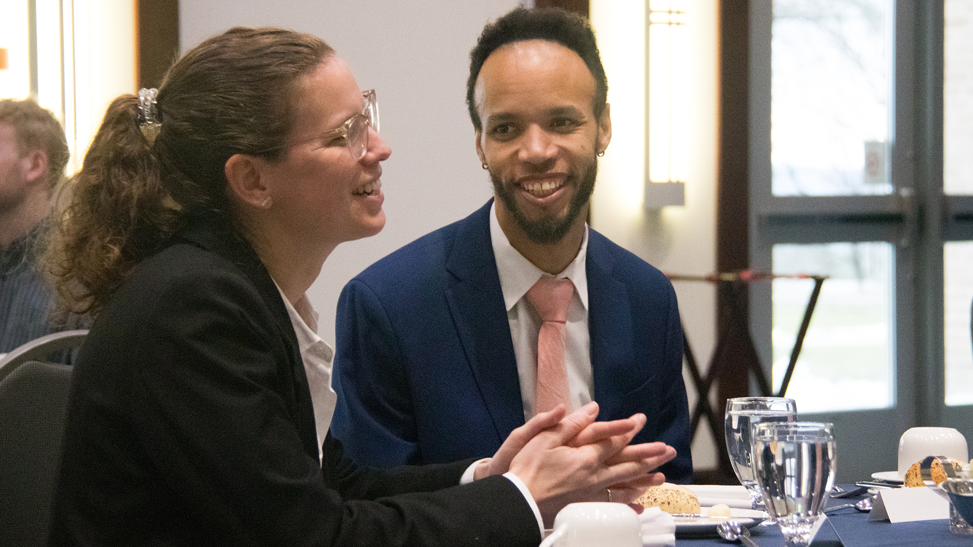 Photo of Chris Payne smiling and listening to another student talk while sitting at a dining table.