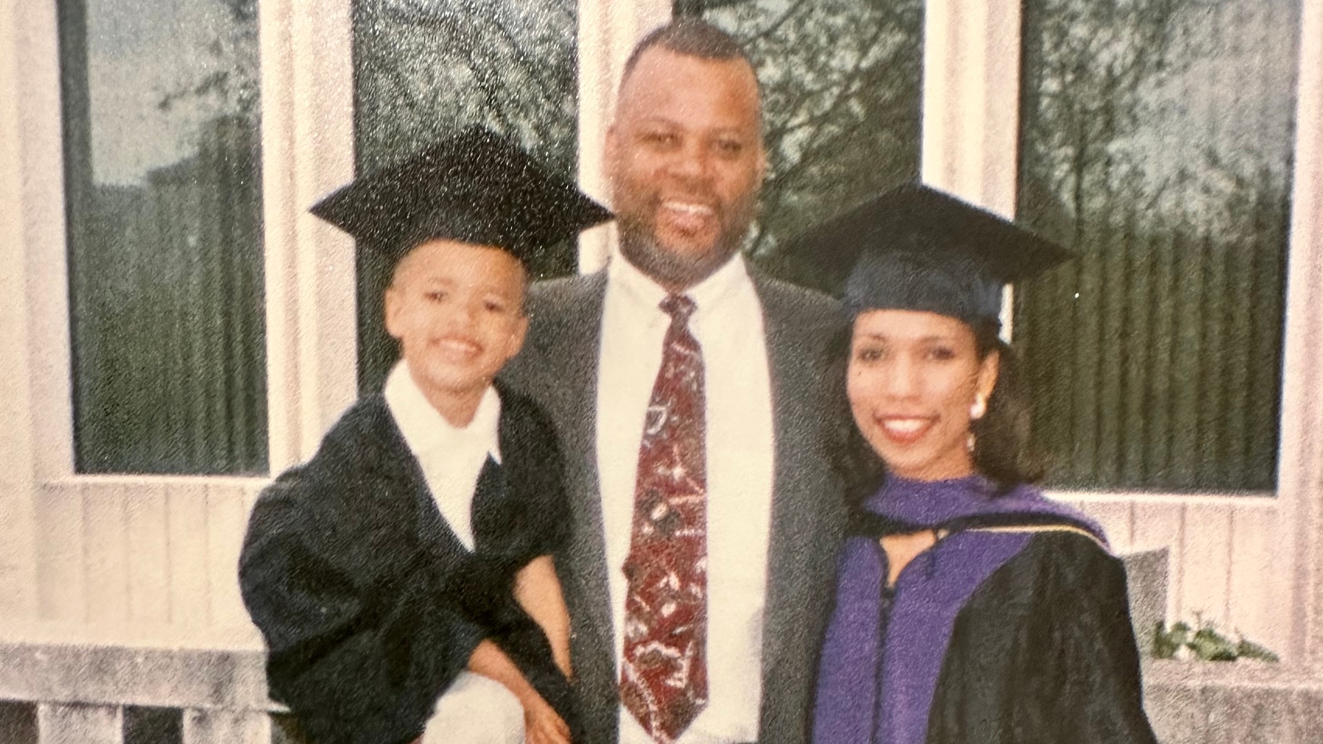 Photo of Chris Payne, as a child, being held by his mother and father. His mother is in graduation regalia.