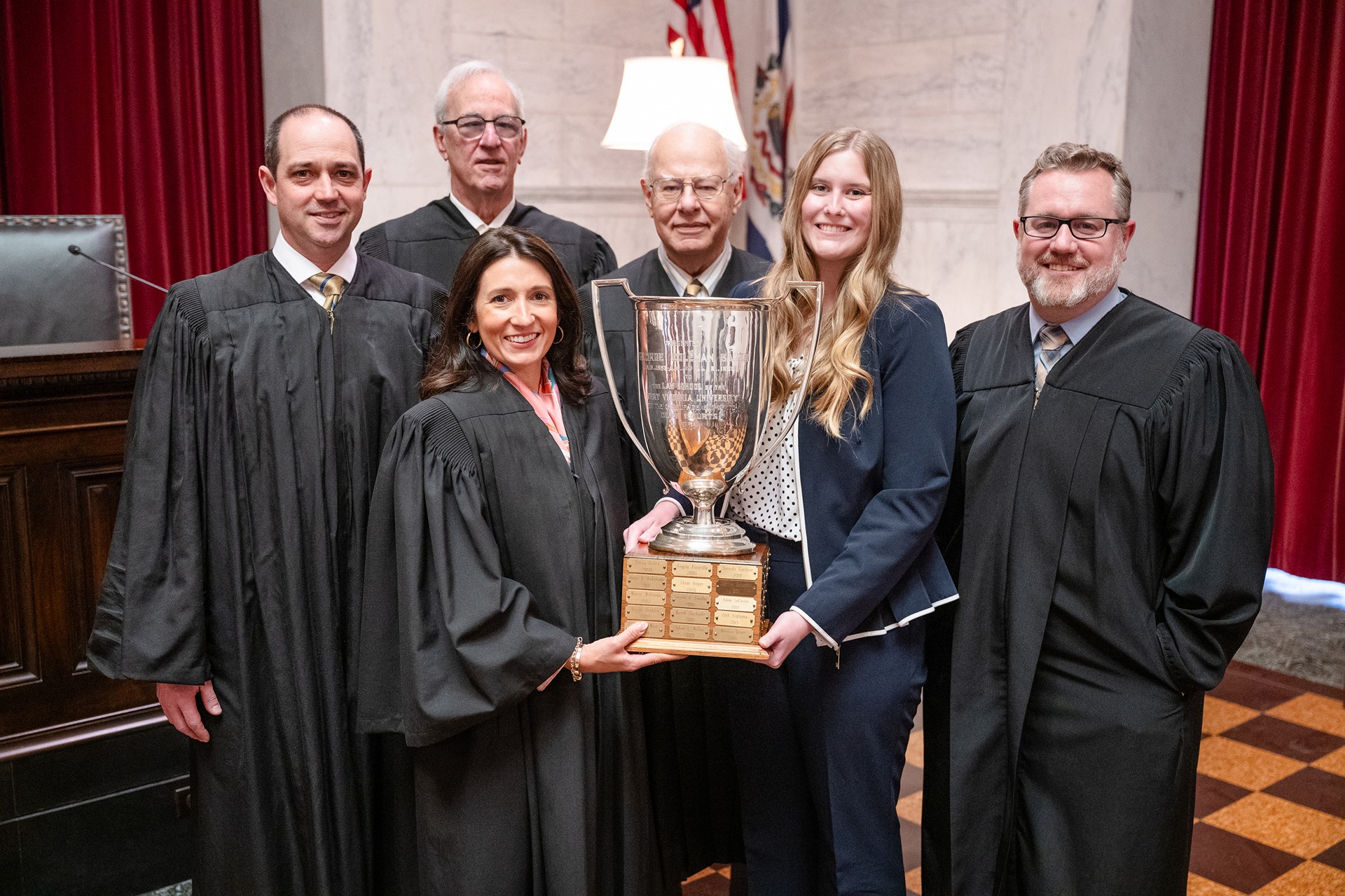 Photo of WVU Law student Kelli Campbell holding the Baker Cup with the justices of the WV Supreme Court.