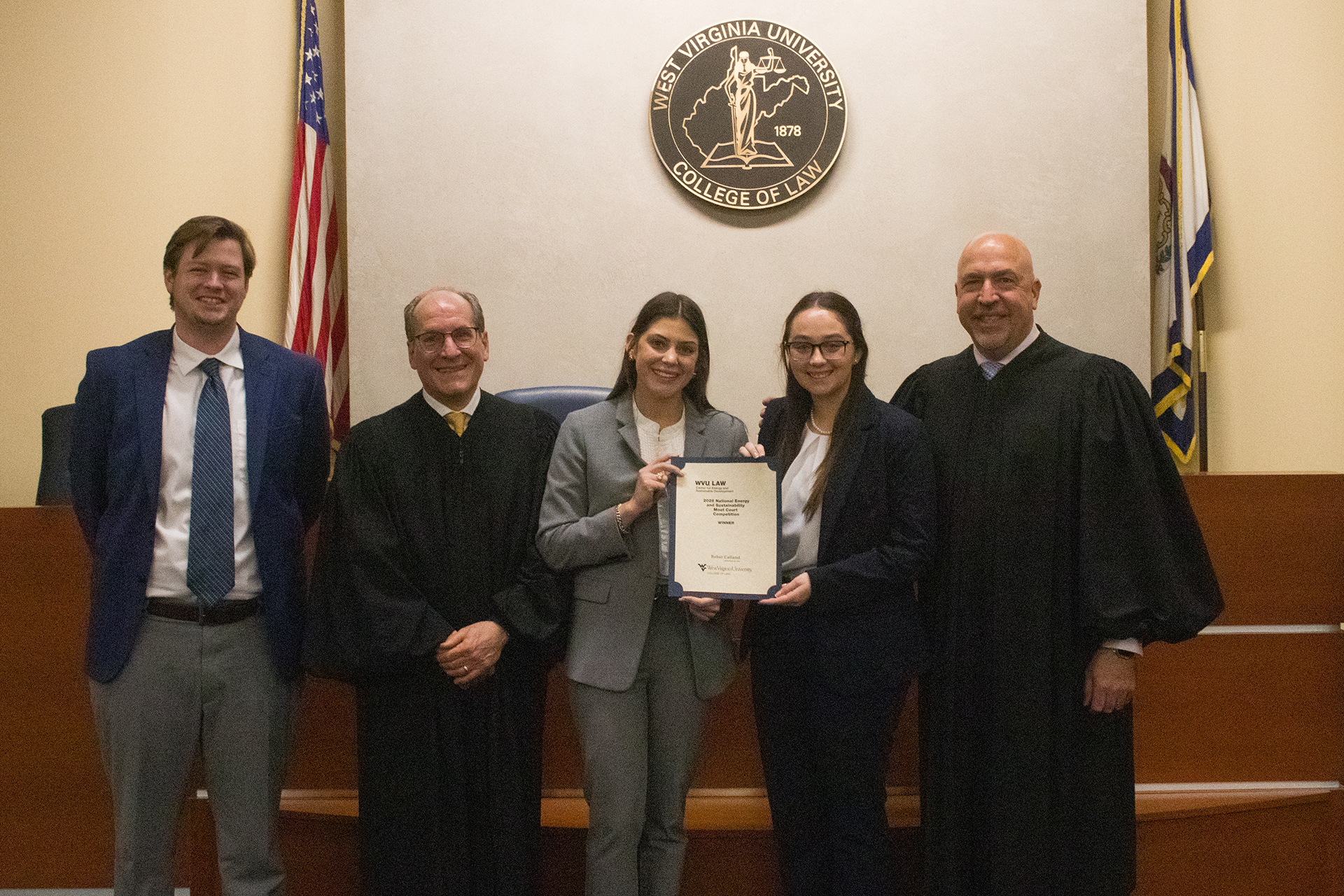 Three College of Law students stand with their Moot Court award next to two court judges.