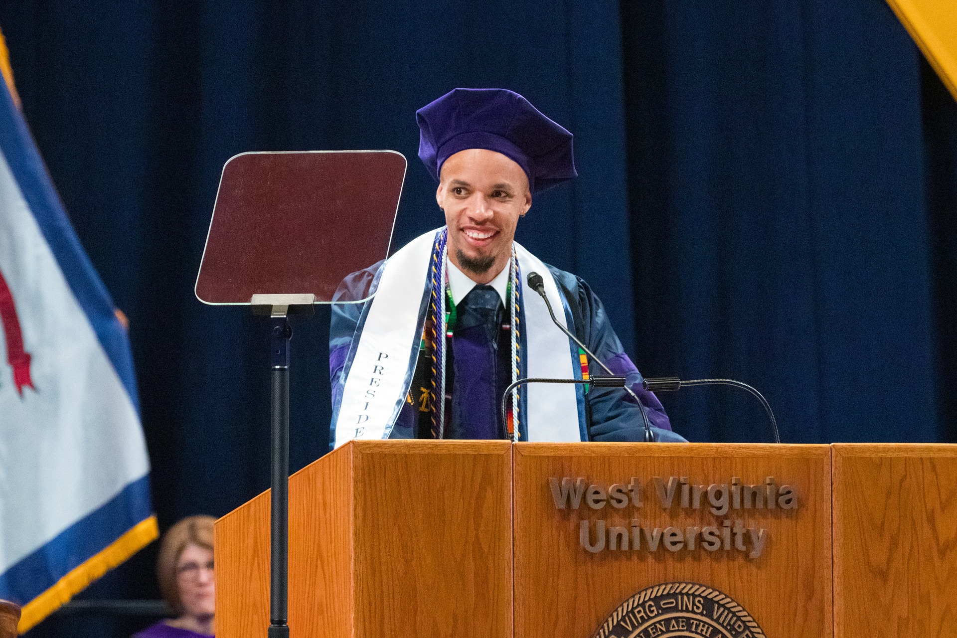 Photo of WVU Law graduate Chris Payne speaking at a podium in graduation regalia.