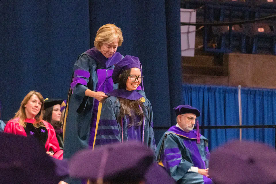 Photo of a WVU Law graduate receiving her hood from Dean Brewer.