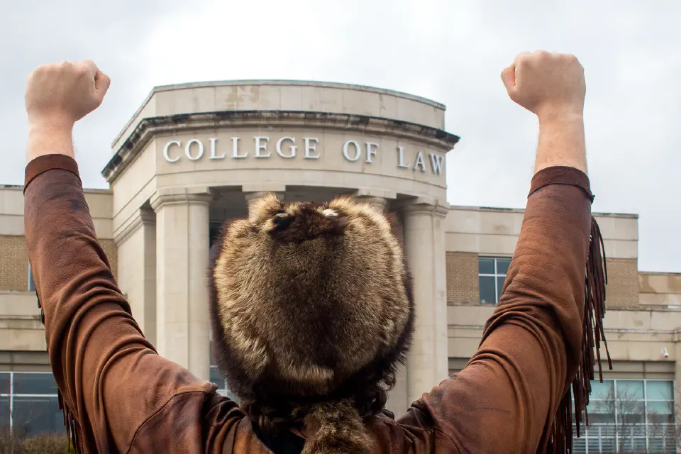 The Mountaineer throws his fists into the air outside the College of Law building.