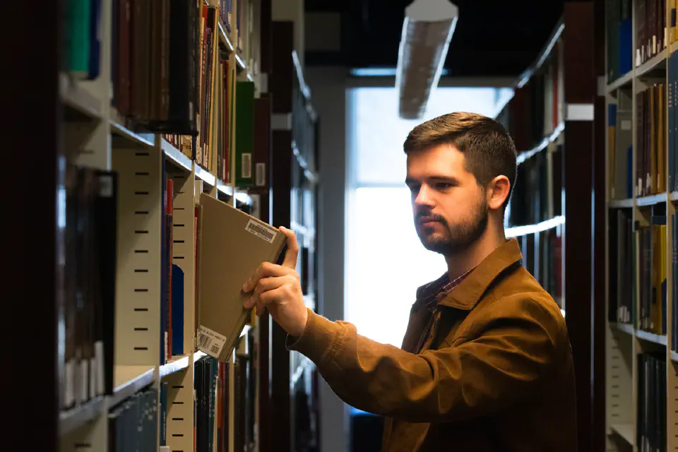 Photo of WVU Law student Grant Joynes pulling a book off the shelf in the WVU Law Library.