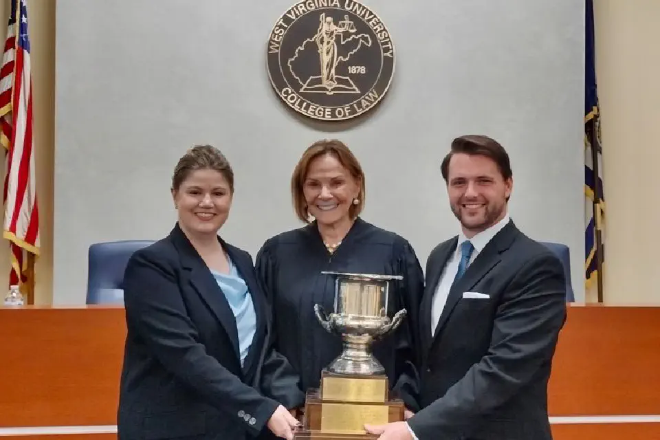 Two students hold the Lugar Cup with the judge in the middle.