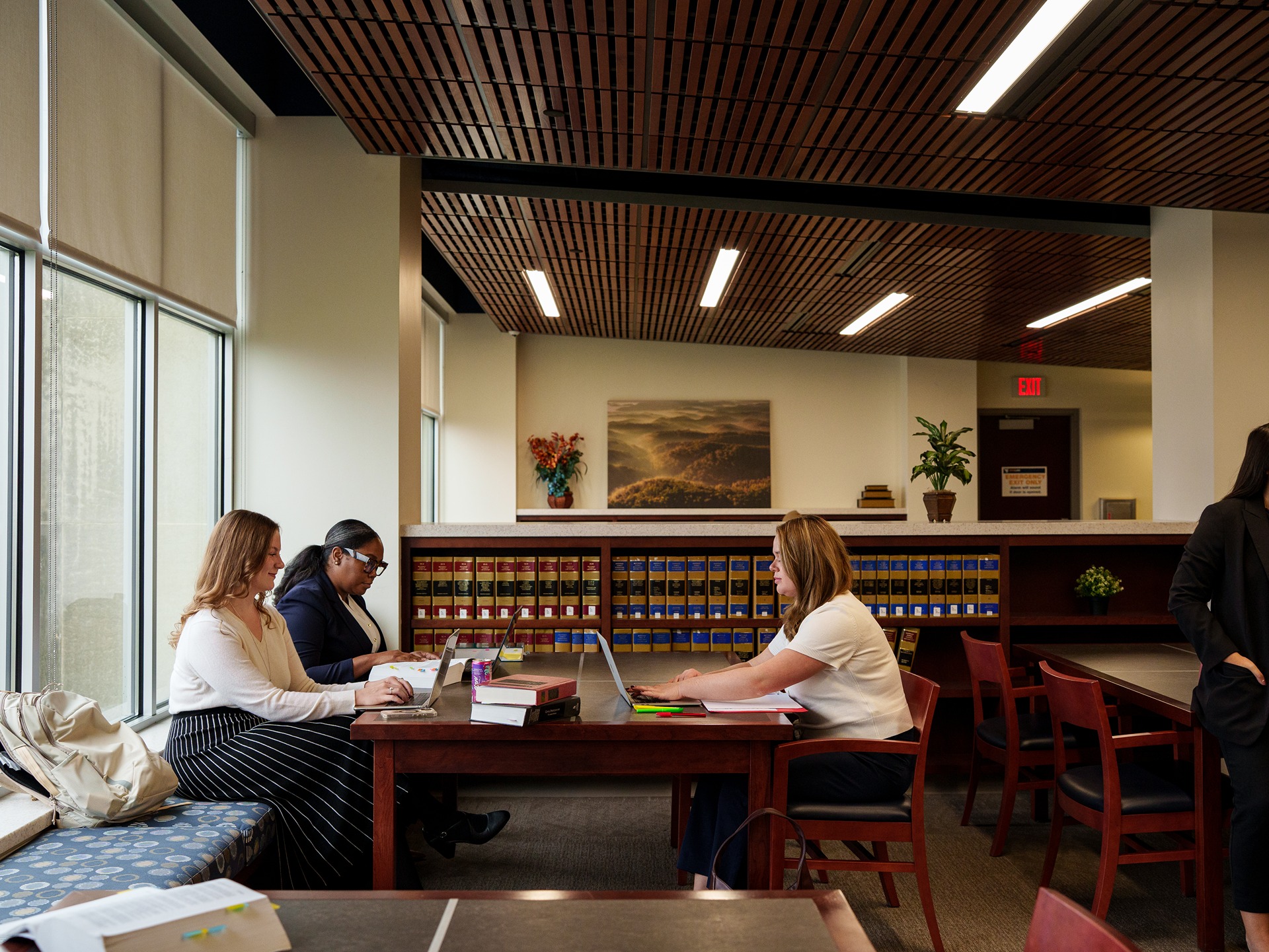Students sit at a table inside the WVU Law library working on laptops.