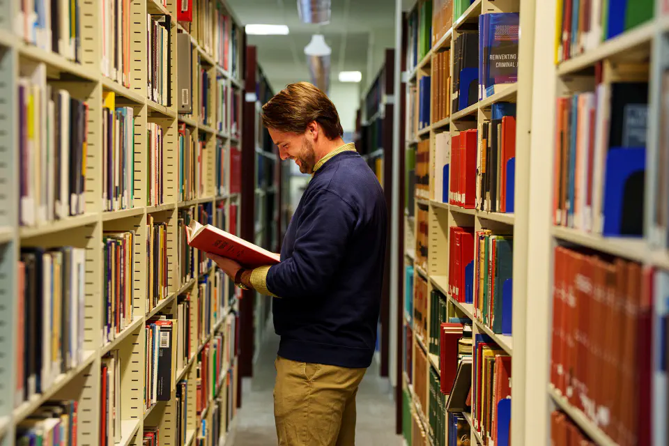 WU Law students stands by bookshelves in the WVU Law library and reads a book.