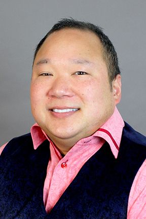 A portrait of Professor Tu wearing a pink collared shirt and black vest.